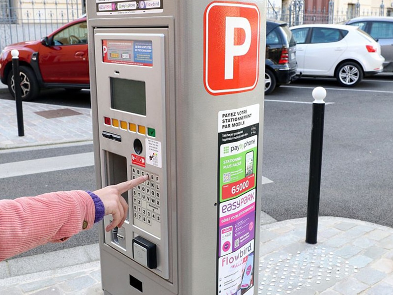 Une personne est en train de prendre un ticket de stationnement à l'horodateur près de la mairie de Tarbes