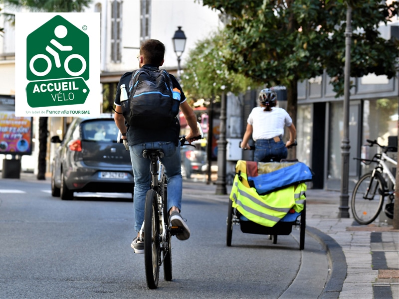 Scène de la rue Maréchal Foch avec 2 cyclistes sac à dos + carriole et le logo Accueil Vélo©
